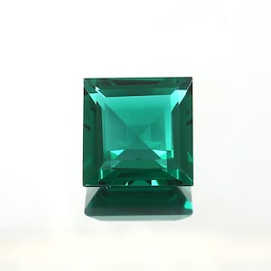 May include: A square cut emerald green gemstone with a faceted design.