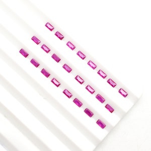 Op de afbeelding: Rijen helder roze, rechthoekige edelstenen worden getoond op een witte ondergrond. De edelstenen zijn gelijkmatig verdeeld en reflecteren licht, wat wijst op een hoogwaardige slijping. De opstelling impliceert een focus op sieraden of edelsteenmaterialen.