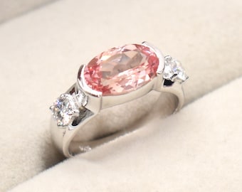May include: A silver ring with a large oval pink gemstone and two smaller round white gemstones on the sides.