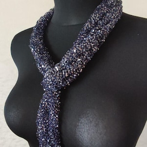 May include: A navy blue scarf with silver sequins is draped on a black mannequin. The scarf is knotted at the neck and hangs down. The scarf is made of a soft, flexible material.