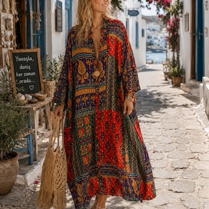 May include: A long, loose-fitting dress featuring a vibrant patchwork pattern in shades of red, blue, green, and yellow with paisley and floral motifs. The garment has long sleeves, a V-neckline, and a button-down front, paired with a tan woven tote bag.