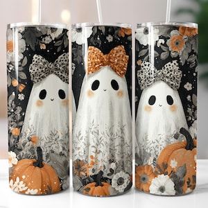 May include: Three cylindrical tumblers featuring a repeating pattern of white ghosts with leopard print bows, orange pumpkins, and black and white floral accents. Each tumbler includes a clear straw and a metal lid, showcasing a festive autumn theme.
