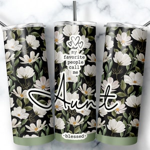 Peut inclure: Un gobelet à fleurs blanches et vertes avec le texte "my favorite people call me Aunt" et "blessed" en bas.