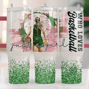 May include: A white stainless steel tumbler with a pink and green watercolor design featuring a basketball player. The tumbler has a pink lid and handle. The text "Who Loves Basketball" is printed on the side of the tumbler.