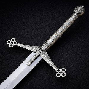 May include: A silver-toned sword featuring an intricate crossguard with four-ringed terminals and a textured, patterned hilt. The handle includes detailed metalwork, a pommel with a central emblem, and a straight, polished steel blade.