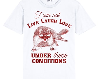 May include: White t-shirt with a red raccoon illustration and the text "I can not LIVE LAUGH LOVE UNDER these CONDITIONS".