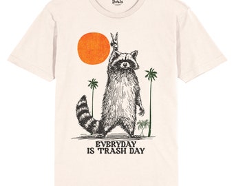May include: A cream colored t-shirt with a black and white illustration of a raccoon giving the peace sign. The raccoon is standing in front of a large orange sun and palm trees. The text "EVERYDAY IS TRASH DAY" is printed below the raccoon.