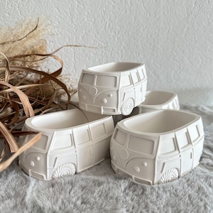 Könnte beinhalten: Vier weiße Keramik-Blumentöpfe in Form von Vintage-Volkswagen-Transportern. Die Töpfe sind alle gleich groß und haben eine glatte, matte Oberfläche.