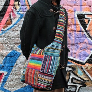 May include: A colourful patchwork shoulder bag with a long strap. The bag is made of different fabrics with geometric patterns in shades of blue, red, yellow, and green.