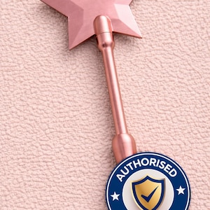 May include: A rose gold star-shaped wand with a long handle. The wand has a metallic finish and is positioned diagonally on a textured pink surface. An "AUTHORISED SELLER" badge is at the bottom.