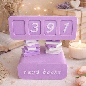 May include: A lavender-colored book counter with the numbers 397 displayed. The counter is supported by stacks of miniature books. The base of the counter reads "read books". The background includes a lit candle and decorative elements.