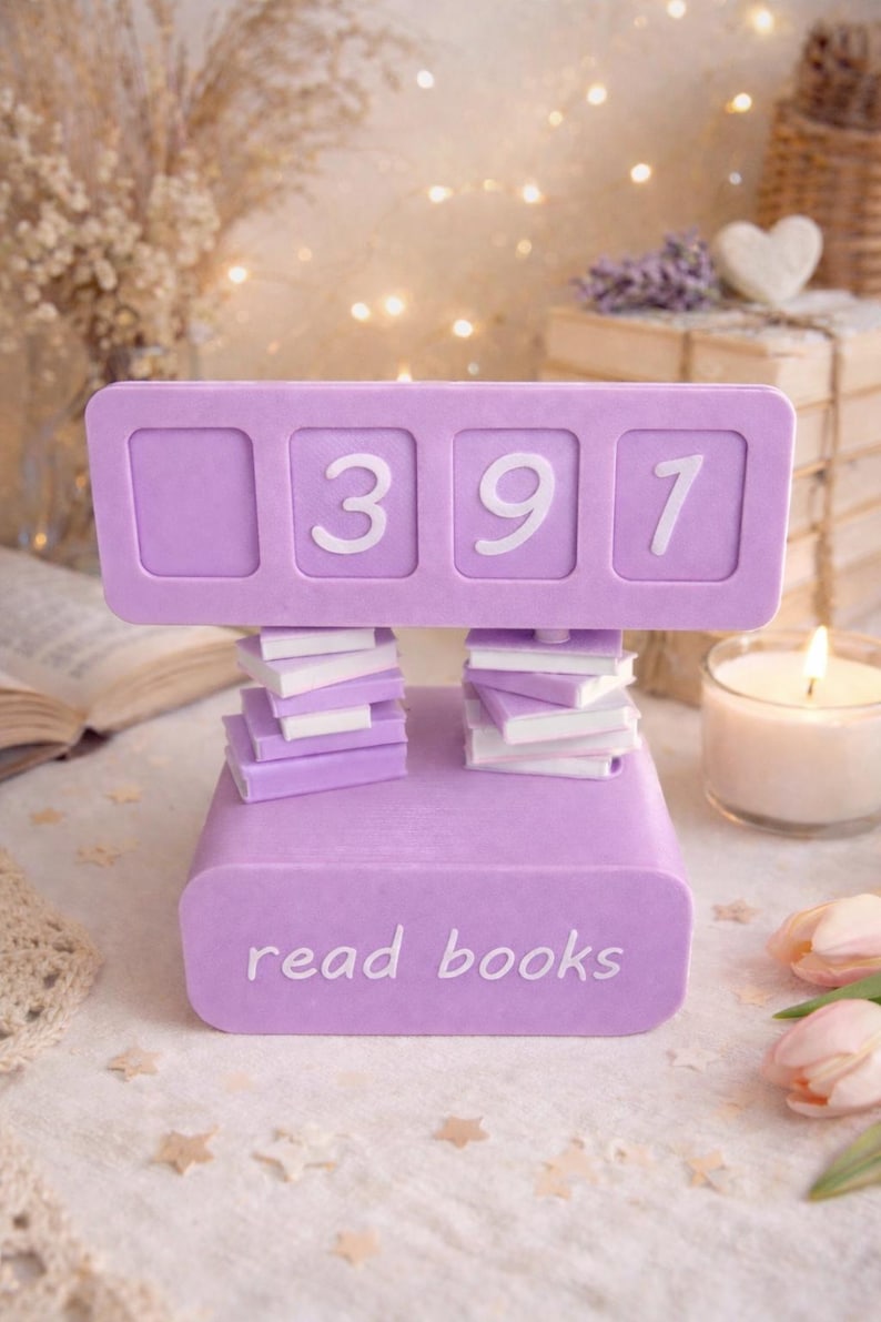 May include: A lavender-colored book counter with the numbers 397 displayed. The counter is supported by stacks of miniature books. The base of the counter reads "read books". The background includes a lit candle and decorative elements.