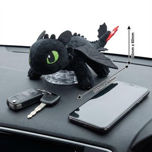 May include: A black plush dragon toy with green eyes and red tail accents sits on a clear plastic base. The toy is next to a set of car keys and a smartphone. The dimensions of the phone are 175mm x 60mm.