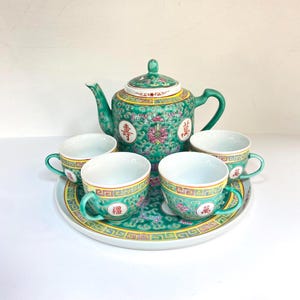 May include: A vintage porcelain tea set in green, yellow, and white. The set includes a teapot, four teacups, and a serving tray. The teapot and cups feature floral and Chinese character designs.