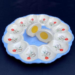 Peut inclure: Un plat de service à œufs farcis vintage avec un bord festonné bleu clair et des compartiments individuels pour les œufs. Le plat présente des motifs floraux et est associé à deux salières et poivrières en forme d'œuf. Les jaunes d'œufs sont jaune vif.