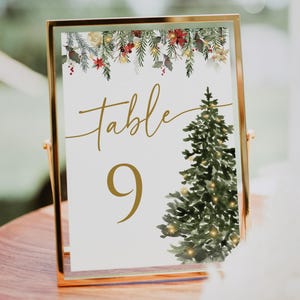 May include: A gold-framed table number card with the word "Table" in gold script and the number "9" in gold. A watercolor Christmas tree is on the right. The top has a floral garland with red berries and green leaves.