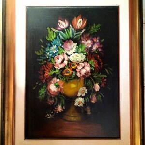 May include: A framed oil painting of a still life featuring a yellow vase overflowing with a variety of colorful flowers, including pink, red, white, and blue blooms. The painting is set against a dark background.
