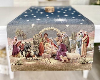 May include: A blue and beige table runner with a depiction of the nativity scene. The scene includes Mary, Joseph, baby Jesus, a donkey, sheep, and a star.