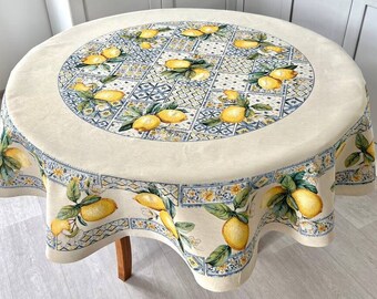 May include: A round tablecloth with a lemon design. The tablecloth has a cream-colored background with a repeating pattern of lemons, green leaves, and blue and yellow decorative tiles. The tablecloth is on a wooden table.