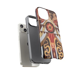 May include: A silver smartphone with a black case and a decorative phone case. The decorative case features a geometric design with red, gold, and brown colors, including a sun and snake motif.