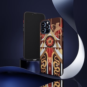 May include: A phone case with a geometric design in red, gold, and white. The case features a central sunburst design, stylized snakes, and a lion figure. A black phone is next to the case, set against a dark blue background.
