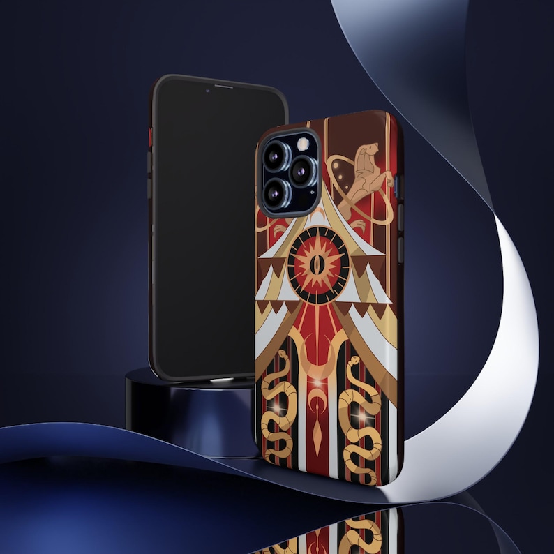 May include: A phone case with a geometric design in red, gold, and white. The case features a central sunburst design, stylized snakes, and a lion figure. A black phone is next to the case, set against a dark blue background.