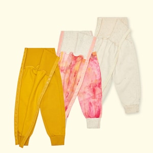 Puede incluir: Tres pantalones de bebé en amarillo mostaza, rosa tie-dye y blanco roto. Los pantalones mostaza tienen un diseño envolvente con ribete decorativo. Los pantalones tie-dye tienen un estampado rosa y blanco. Los pantalones blanco roto tienen un diseño moteado.