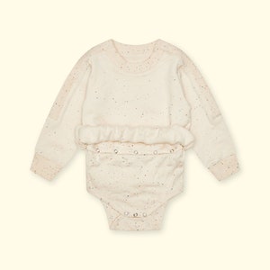 Peut inclure: Une grenouillère bébé à manches longues de couleur crème avec un motif moucheté de différentes couleurs. La grenouillère a une fermeture à pression à l'entrejambe et un col rond.