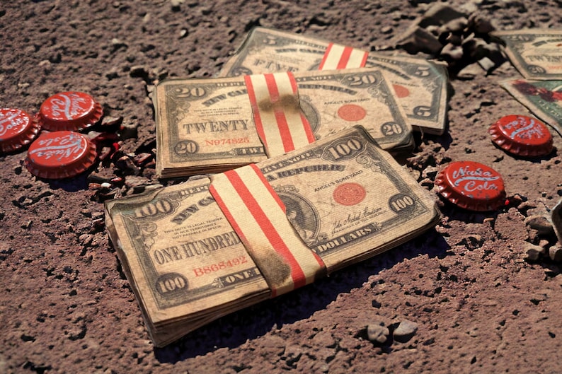 K&ouml;nnte beinhalten: Ein Stapel alter, abgenutzter US-Dollar-Scheine, darunter ein 100-Dollar-Schein und mehrere 20-Dollar-Scheine, sind mit einem rot-wei&szlig; gestreiften Band zusammengebunden. Die Scheine liegen auf einer schmutzigen Oberfl&auml;che mit mehreren roten Flaschenverschl&uuml;ssen, die herumliegen.