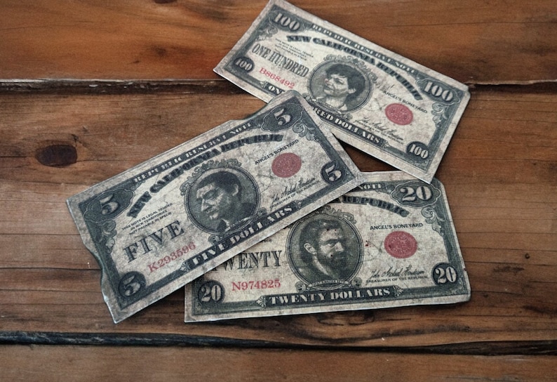 K&ouml;nnte beinhalten: Vier Banknoten im Vintage-Stil mit roten Siegeln und Portr&auml;ts von Personen. Die Scheine sind im Wert von f&uuml;nf, zwanzig und hundert Euro. Die Scheine liegen auf einer Holzoberfl&auml;che.