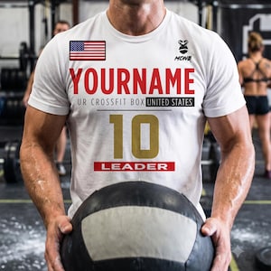 Puede incluir: Una camiseta blanca de manga corta con una bandera de Estados Unidos, un logotipo de gorila con el texto MONQ, y el texto YOURNAME, UR CROSSFIT BOX UNITED STATES, el número 10 en dorado y la palabra LEADER en un recuadro rojo al frente.