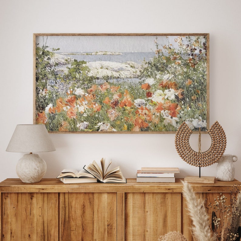 May include: A framed painting of a coastal landscape with a field of wildflowers in shades of orange, pink, and white. The painting is set against a backdrop of a blue ocean and a sandy shore.