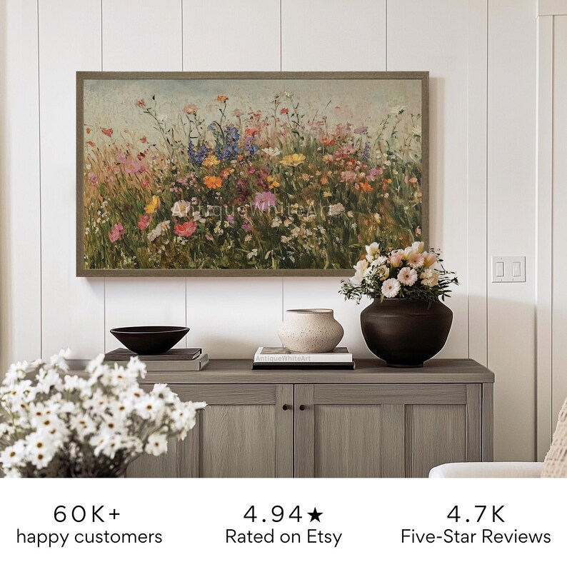 Puede incluir: Una pintura enmarcada de un campo de flores silvestres en tonos de rosa, morado, amarillo y blanco. La pintura est&aacute; colgada en una pared sobre un armario de madera con un jarr&oacute;n de flores y un libro en la parte superior.