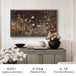 May include: A framed print of a dark floral painting featuring a variety of flowers in shades of pink, red, yellow, and white. The print is hanging on a white wall above a wooden cabinet with a vase of flowers and a bowl.