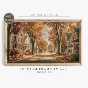 May include: A framed print depicting an autumnal street scene. The artwork shows houses with fall foliage, pumpkins, and the text "ANTIQUE WHITE ART" and "PREMIUM FRAME TV ART". The frame is made of light-coloured wood.