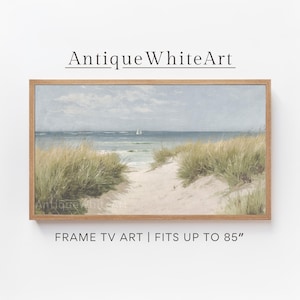 Op de afbeelding: Een ingelijst schilderij van een strandscène met een pad dat door hoog gras naar de oceaan leidt. De lucht is blauw en het water is lichtblauw. In de verte is een klein zeilbootje te zien. De tekst "Antique White Art" staat bovenaan het frame en "FRAME TV ART | FITS UP TO 85" staat onderaan.