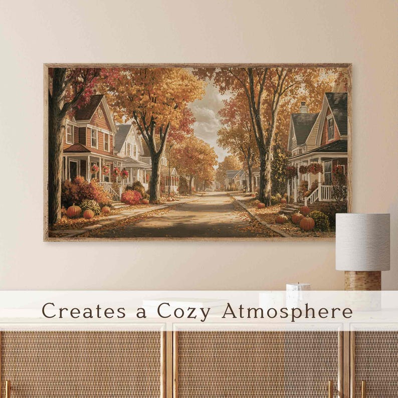 May include: A framed print of an autumnal street scene, featuring houses with porches, trees with golden leaves, and pumpkins. The text at the bottom reads "Creates a Cozy Atmosphere."