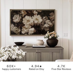May include: A framed painting of white flowers with a dark background. The painting is hanging on a white wall above a wooden cabinet. The cabinet has two doors and two drawers. There are flowers in a vase on the cabinet. The image also includes text that says "60K+ happy customers", "4.94 Rated on Etsy", and "4.7K Five-Star Reviews".