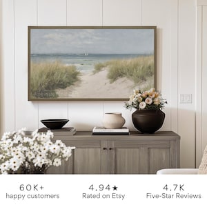May include: A framed painting of a seascape with a path leading to the ocean. The painting is hanging on a white wall above a wooden cabinet with a vase of flowers and a bowl on top. The text "Antique WhiteArt" is visible in the bottom left corner of the painting.