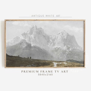 May include: A framed print of a vintage landscape painting depicting a mountain range with snow-capped peaks and a winding path leading into the distance. The painting is in shades of grey and brown, with a light blue sky.