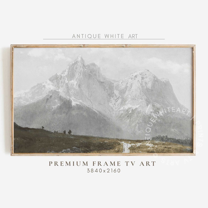 May include: A framed print of a vintage landscape painting depicting a mountain range with snow-capped peaks and a winding path leading into the distance. The painting is in shades of grey and brown, with a light blue sky.