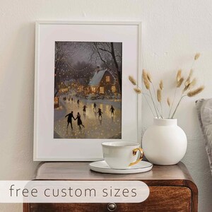 May include: A framed winter scene print of a couple ice skating on a frozen pond with a small house in the background. The print is displayed on a wooden table with a white teacup and saucer.