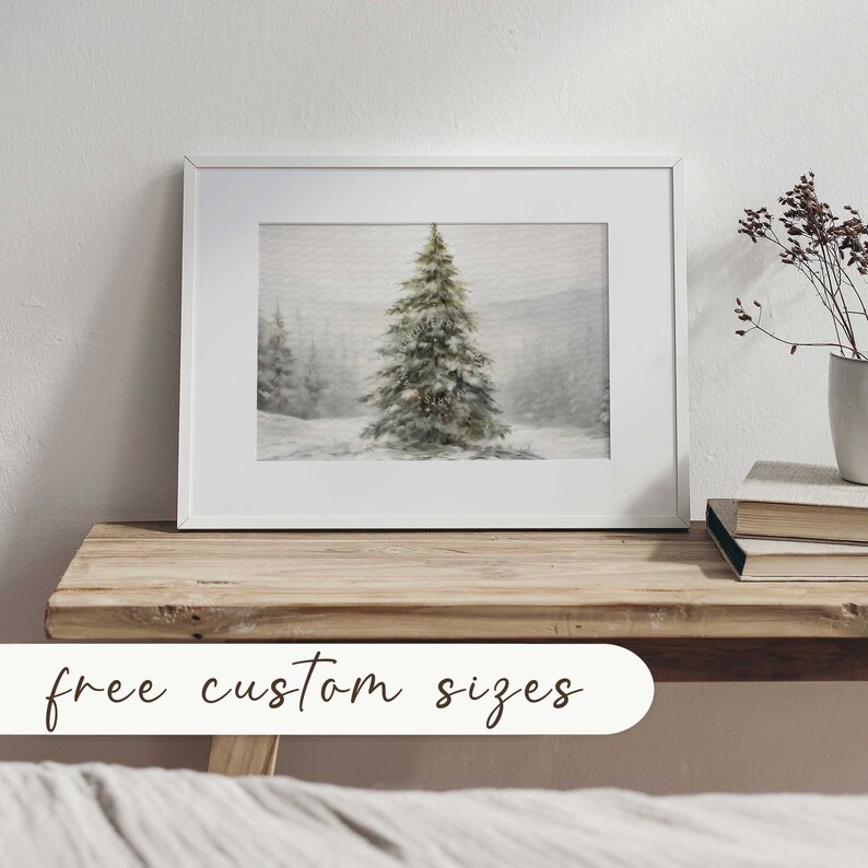 May include: A framed art print depicting a winter scene with a snow-covered fir tree in a snowy forest. The artwork is in a white frame and is displayed on a wooden surface. The text "free custom sizes" is at the bottom of the image.