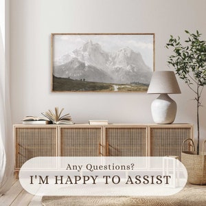 May include: A framed print of a mountain range with snow-capped peaks. The print is hanging on a white wall above a wooden cabinet with woven rattan doors. A white lamp with a beige lampshade sits on the cabinet.