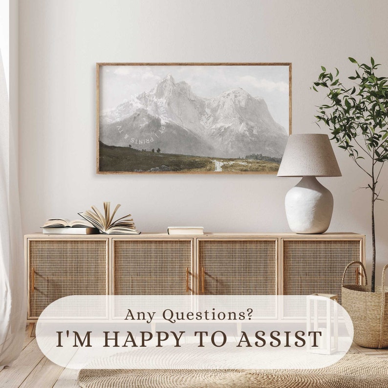 May include: A framed print of a mountain range with snow-capped peaks. The print is hanging on a white wall above a wooden cabinet with woven rattan doors. A white lamp with a beige lampshade sits on the cabinet.