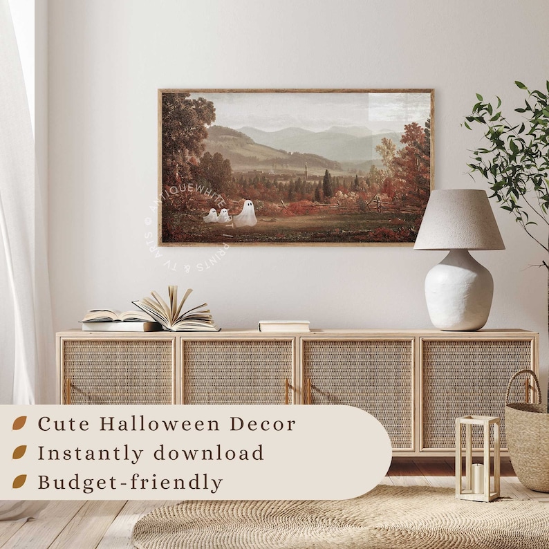 May include: A rectangular wall art print featuring a landscape painting of a valley with mountains in the background and three white ghost figures in the foreground. The print is displayed in a wooden frame on a wall above a light wood cabinet.