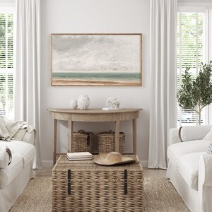 May include: A living room interior with a white couch, a wicker coffee table, and a wooden console table with two wicker baskets. A framed seascape painting hangs on the wall above the console table.
