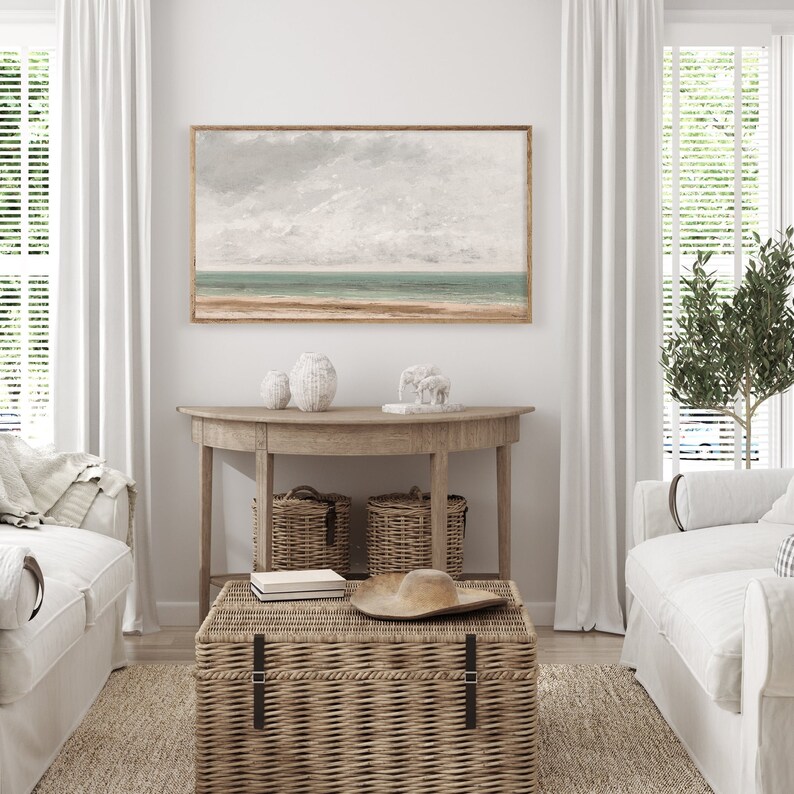 May include: A living room interior with a white couch, a wicker coffee table, and a wooden console table with two wicker baskets. A framed seascape painting hangs on the wall above the console table.