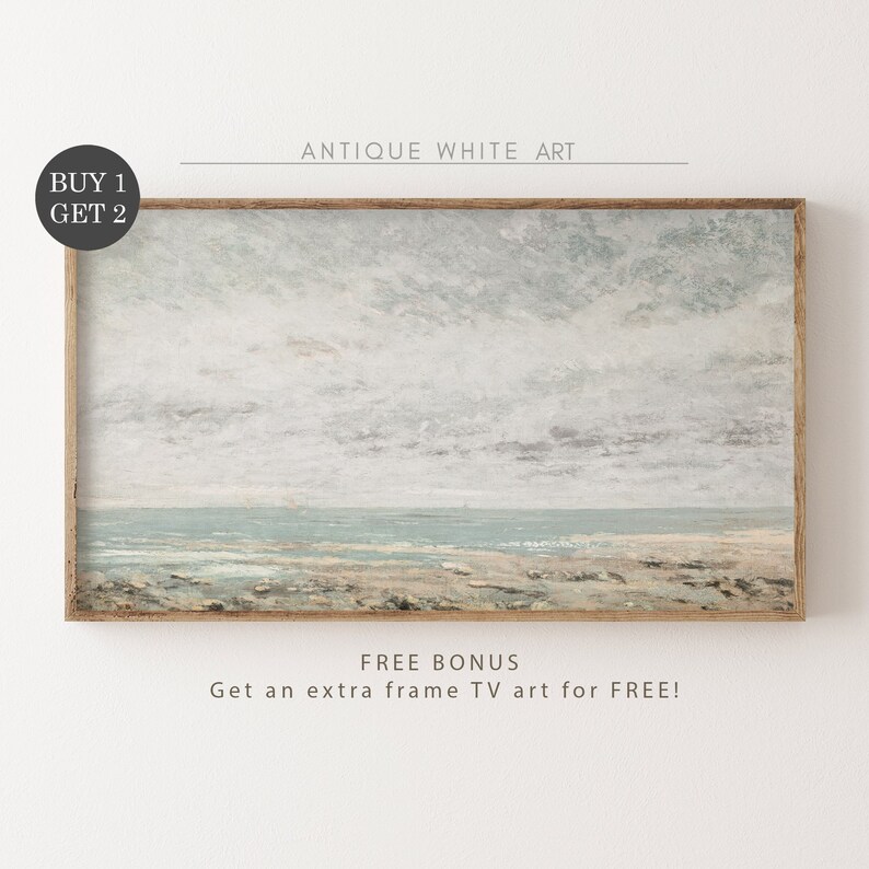 May include: A framed painting of a seascape with a light blue sky and a sandy beach. The painting is in a light wood frame. The text "BUY 1 GET 2" is in the upper left corner of the image. The text "ANTIQUE WHITE ART" is in the upper center of the image. The text "FREE BONUS Get an extra frame TV art for FREE!" is in the lower center of the image.