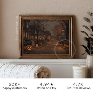 May include: A framed vintage Halloween print depicts a spooky street scene with jack-o'-lanterns and houses. The artwork is in a gold frame and is displayed on a white surface. The print has the text "Antique White Art" on the side.